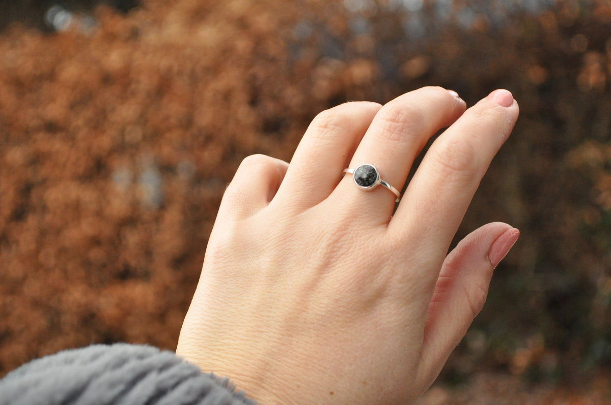 Hand wearing a bespoke sterling silver ashes ring with a dark round memorial inclusion, photographed outdoors in warm natural light