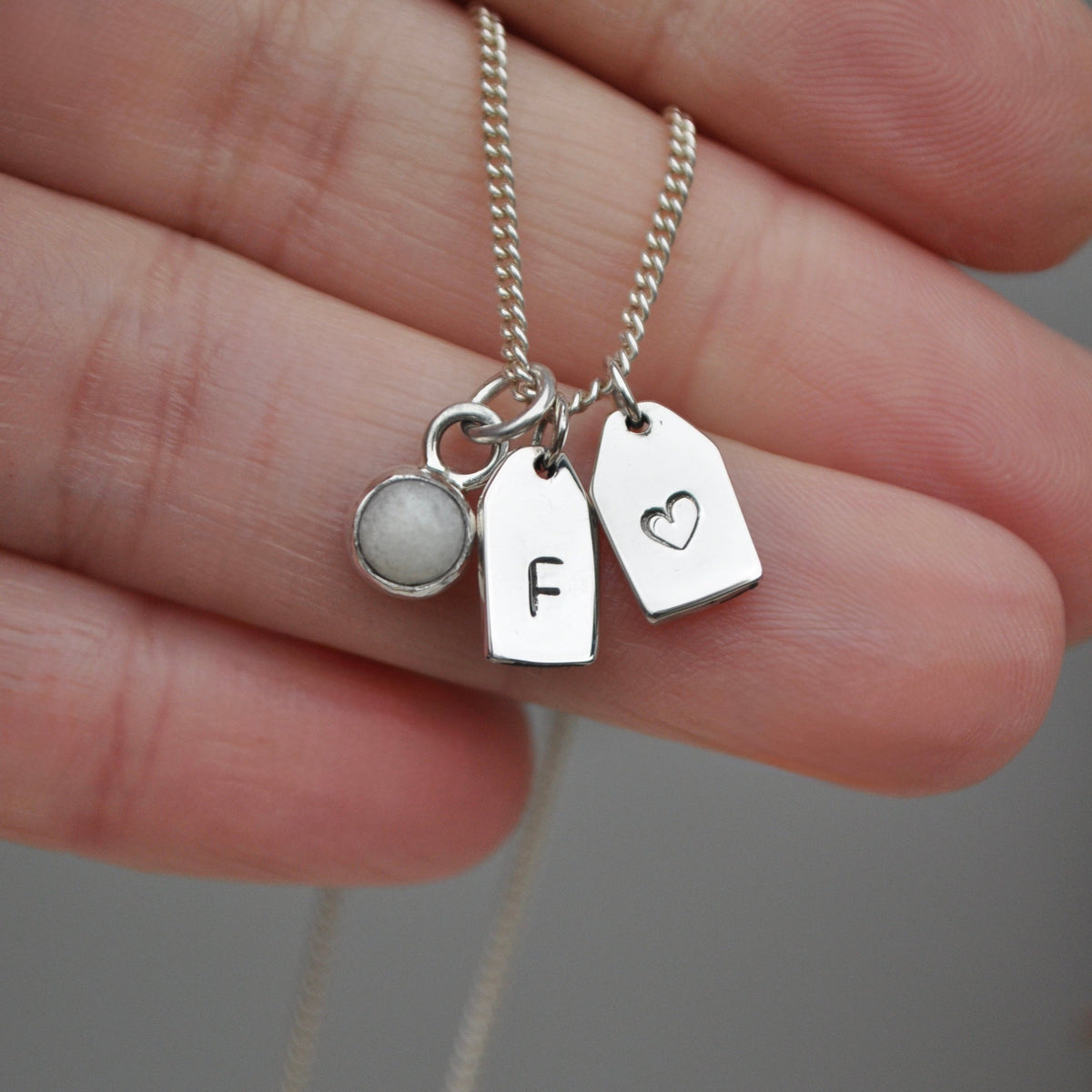 Silver breastmilk necklace with personalised name tags held between fingers against a neutral background