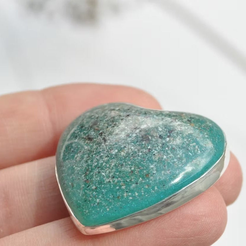 Heart-shaped turquoise cremation keepsake stone held in a hand against a white background