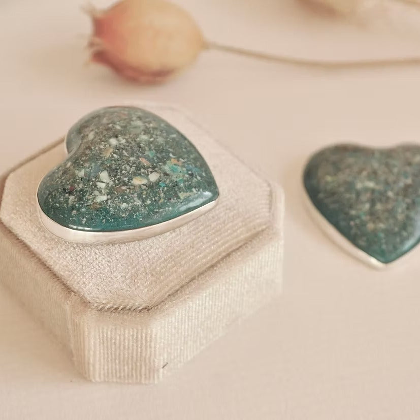Heart-shaped green keepsake stone with ashes in a decorative box on a soft beige background
