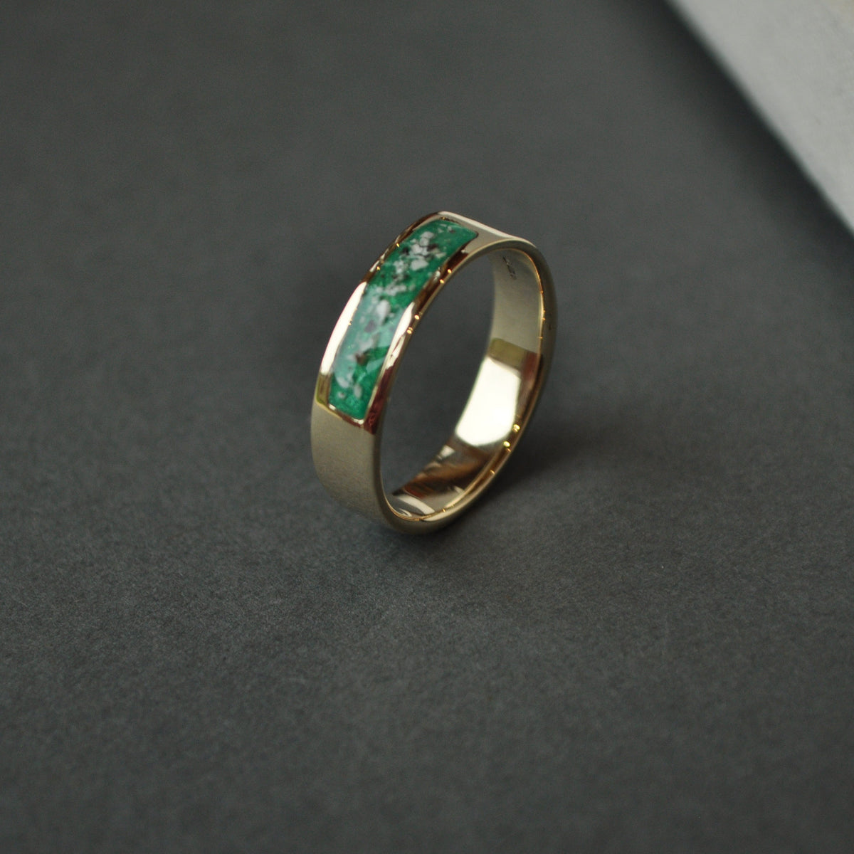 Gold ring with green gemstones made with ashes on a dark surface