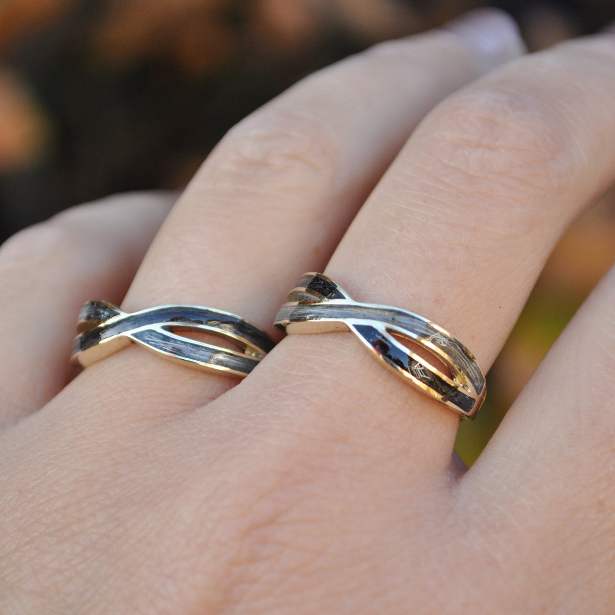 Hand wearing two intertwined gold rings containing horse hair with a blurred natural background