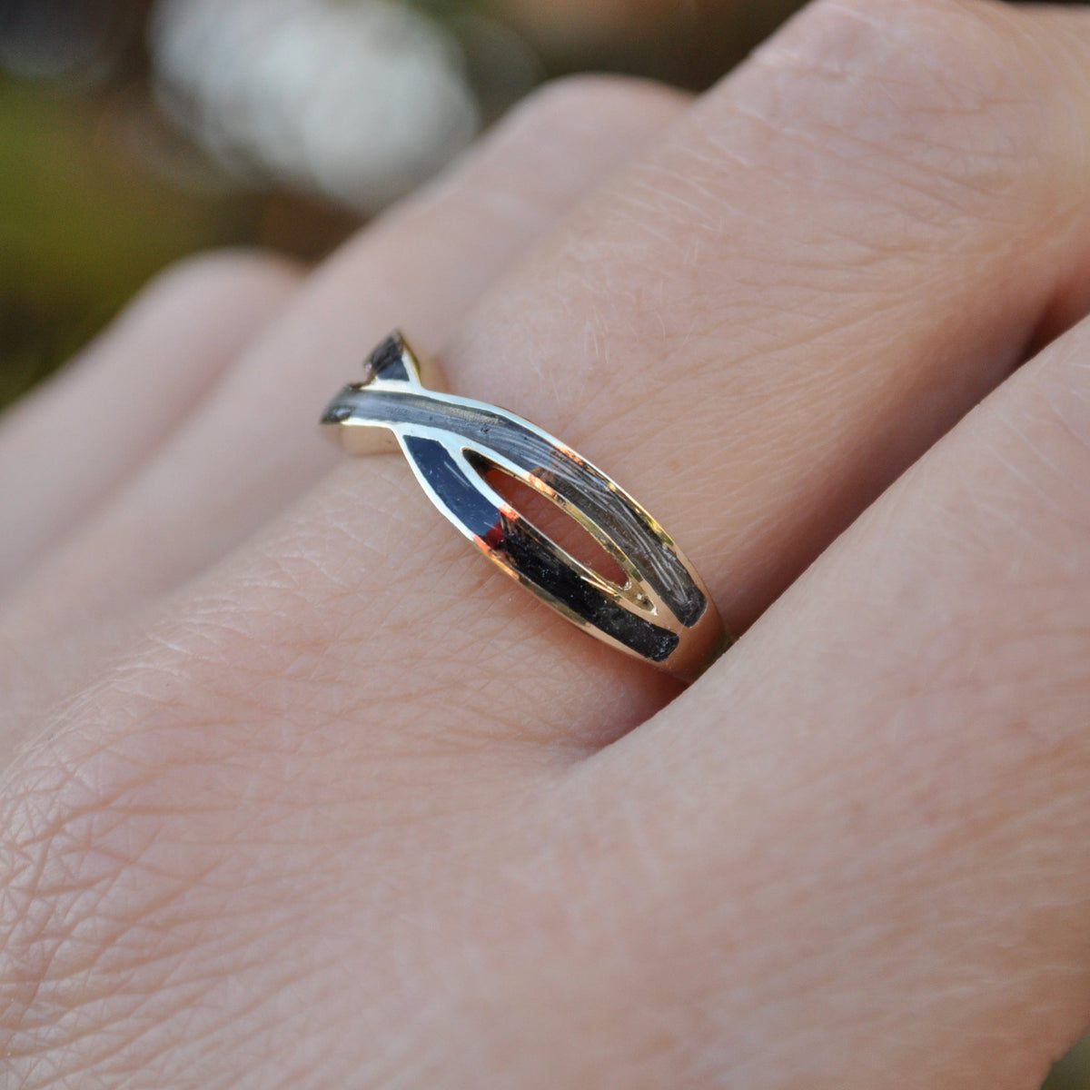 Gold infinity ring with horse hair on person's finger against a blurred natural background