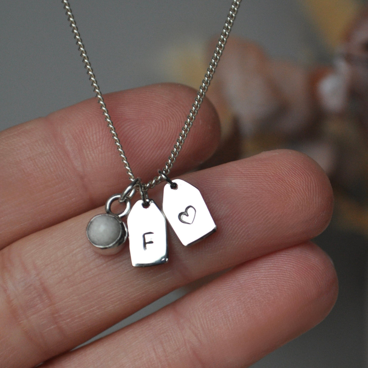 Silver tag necklace with breastmilk charm held by a hand against a blurred background