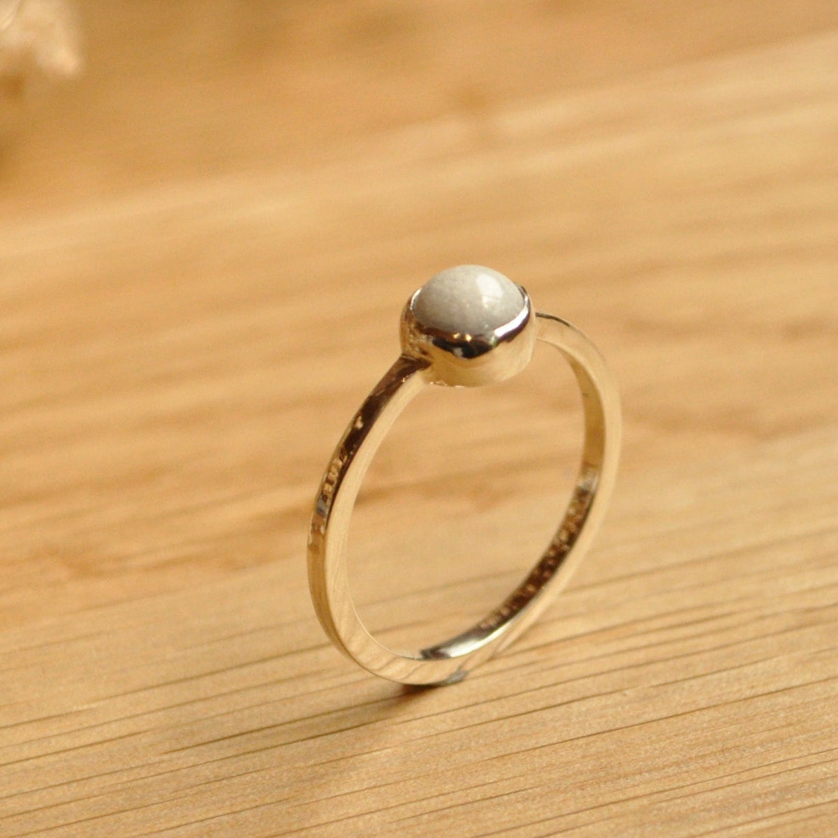 Silver ring with a small round breastmilk stone on a wooden surface with dried flowers.