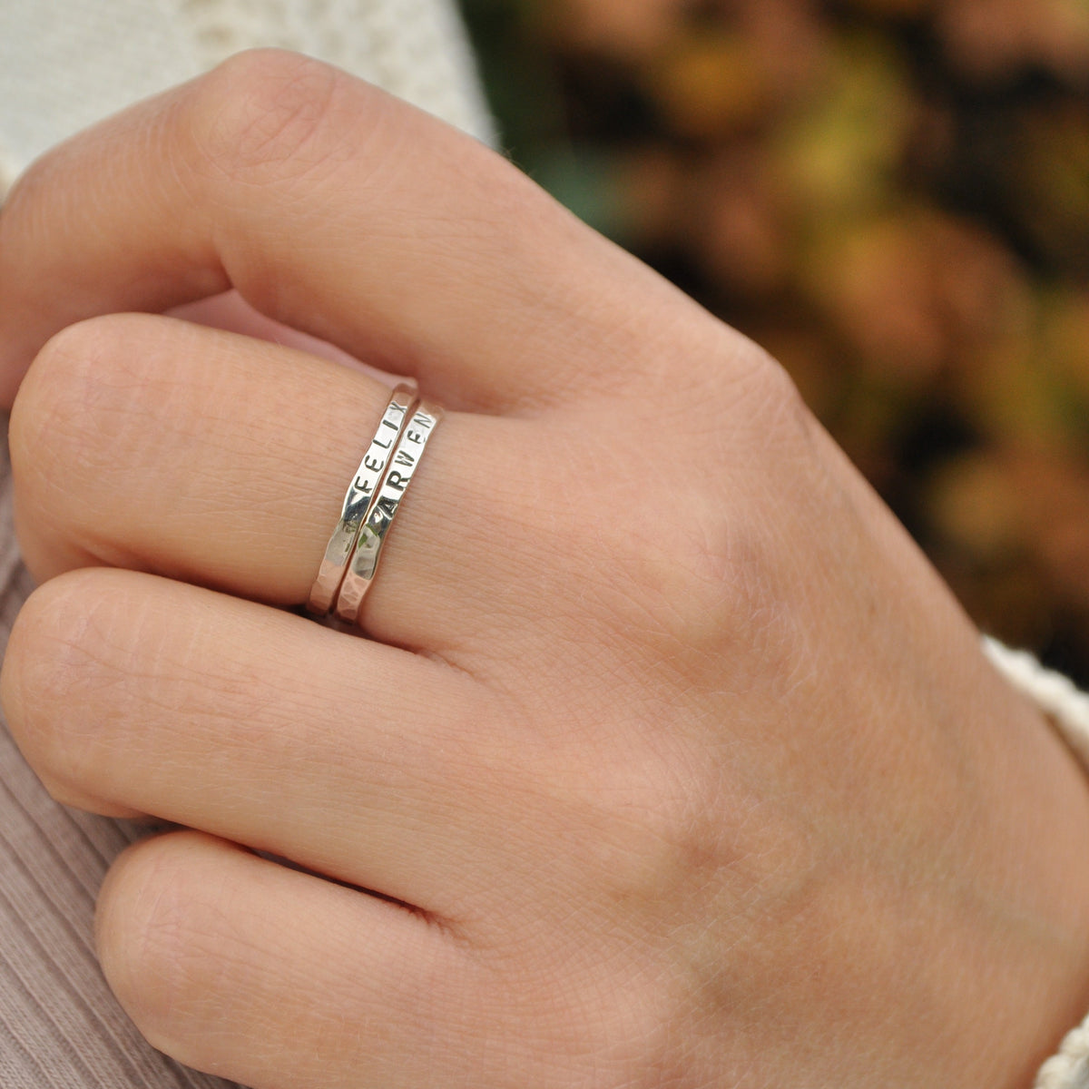 Close-up of a hand wearing two silver rings with names engraved with a blurred natural background