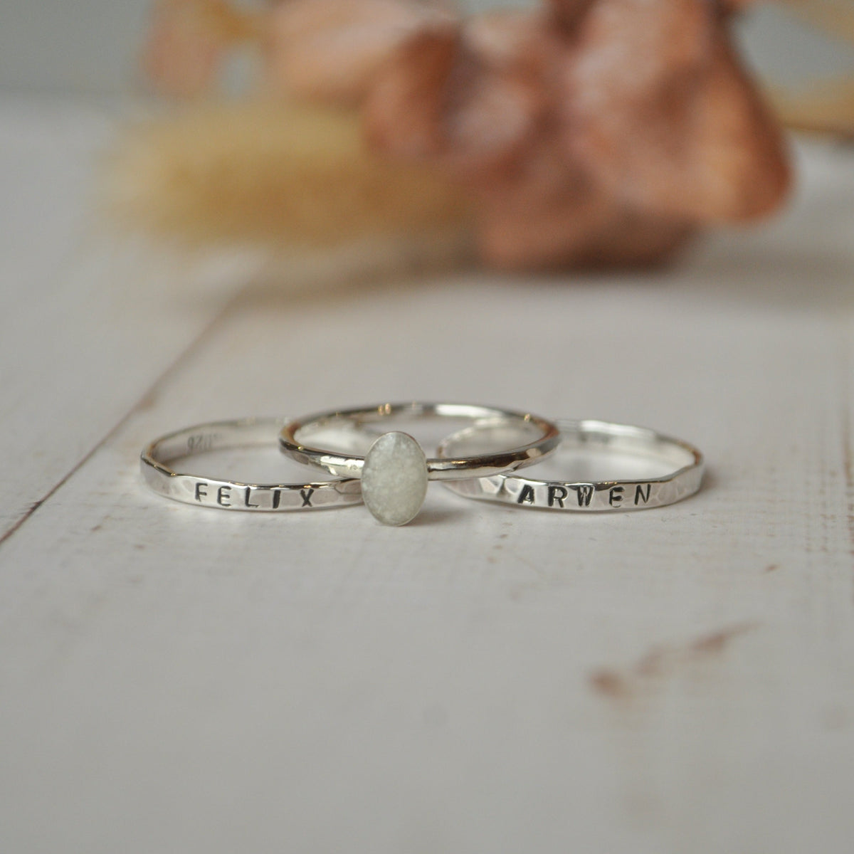 Two silver rings with engraved names on a wooden surface.