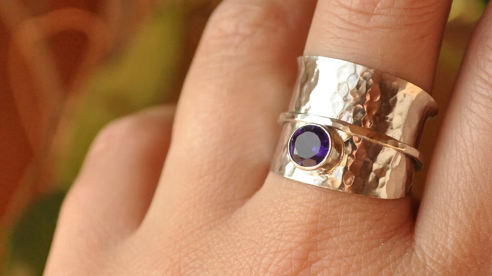 Silver ring with a purple gemstone on a finger against a blurred background