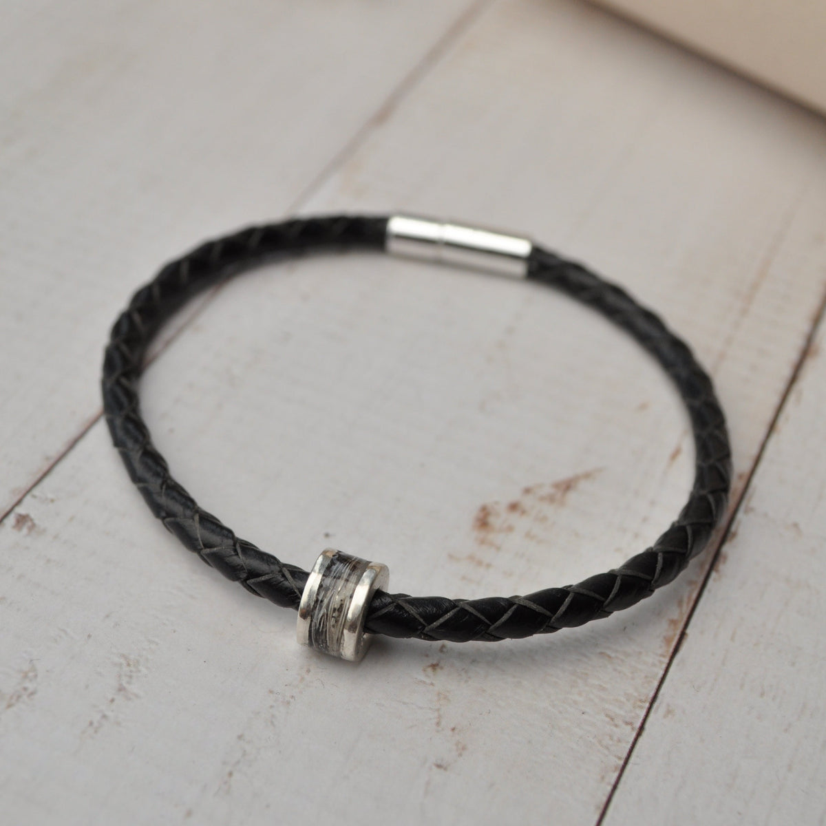 Black braided leather bracelet with silver horse hair charm on a wooden surface