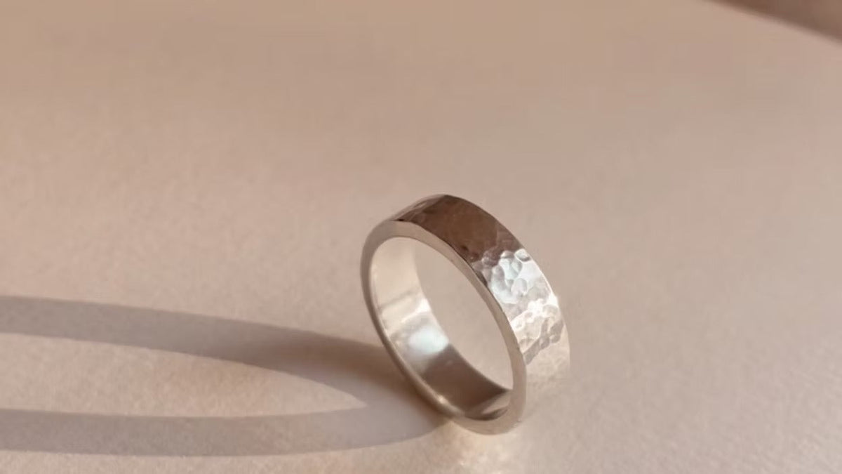 Silver ring with a textured band on a beige background