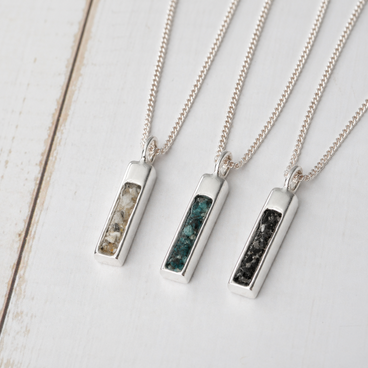Three long silver memorial pendants with clear, teal and black inlays, individually made to hold ashes