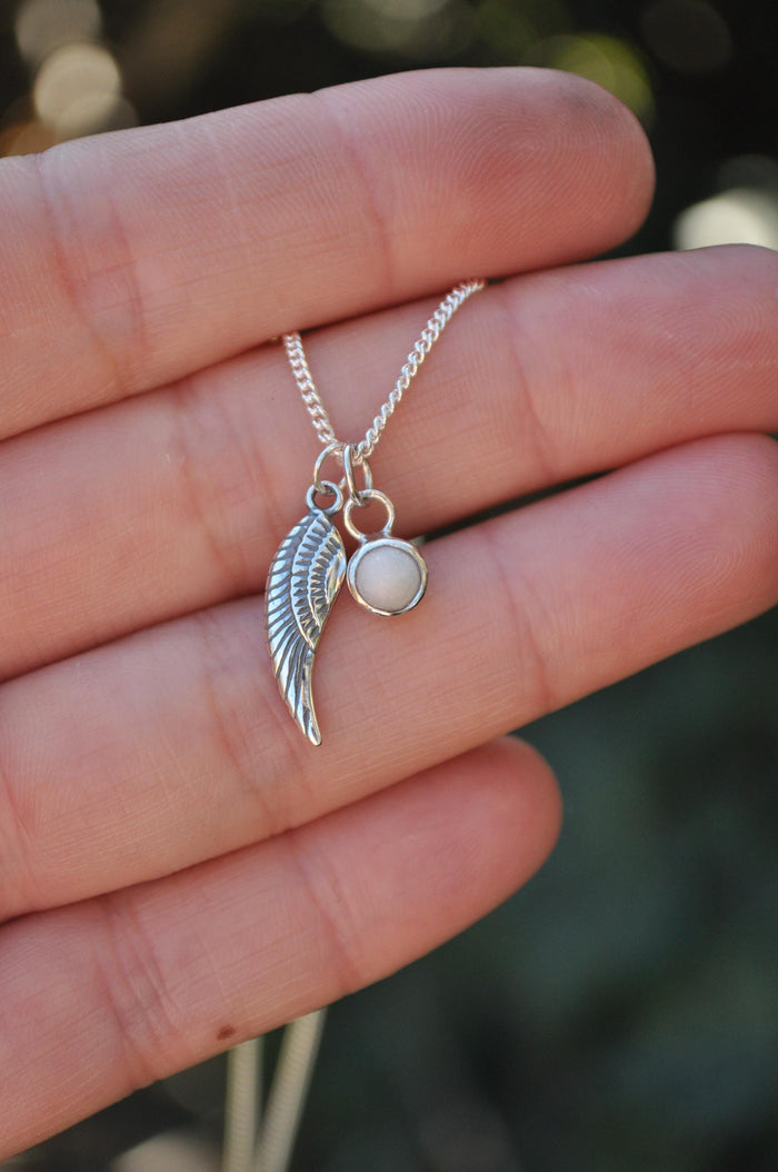 Sterling silver angel wing and breastmilk pendant necklace held in a hand | Mila Faith
