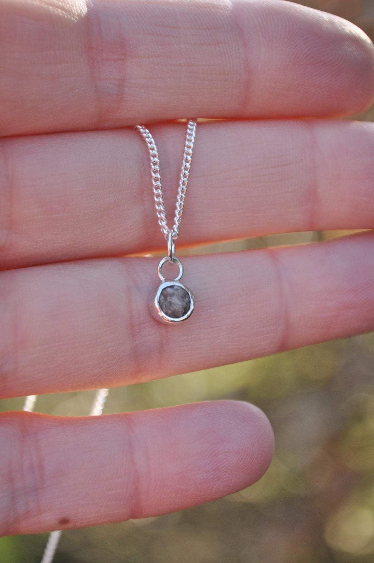Mini round 6 mm memorial ashes pendant held in a hand | Mila Faith