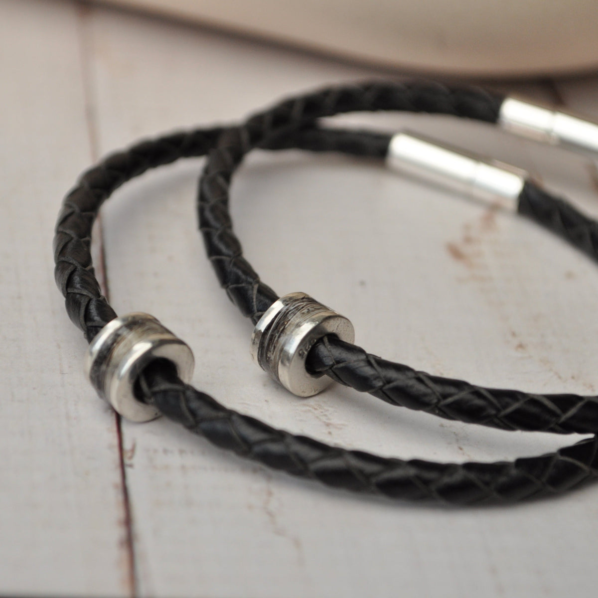 Black braided leather bracelet with horse hair memorial silver beads on a light wooden surface