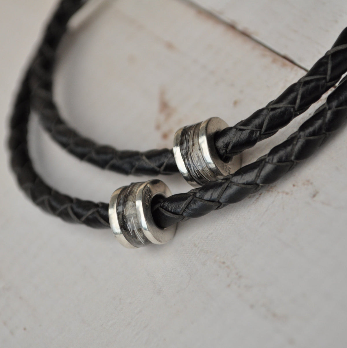Black leather cord with silver horse hair charms on a light wooden surface