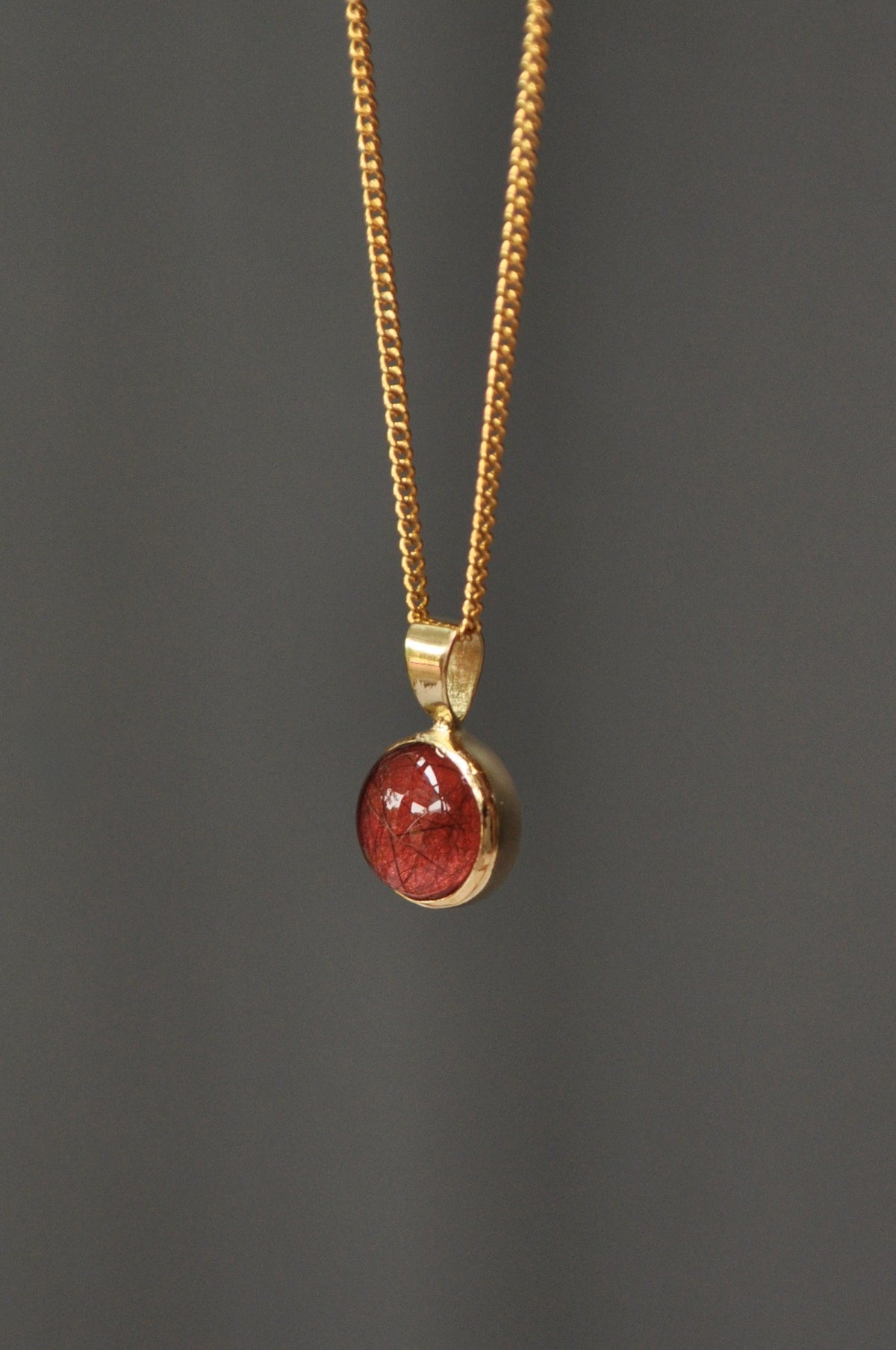 Gold cremation ashes pendant necklace with a round red inlay.