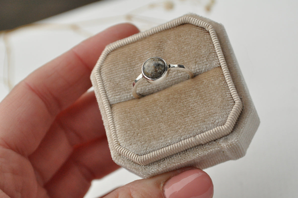 Bespoke sterling silver ashes memorial ring with a round inclusion, presented in an open ivory velvet ring box held in a hand