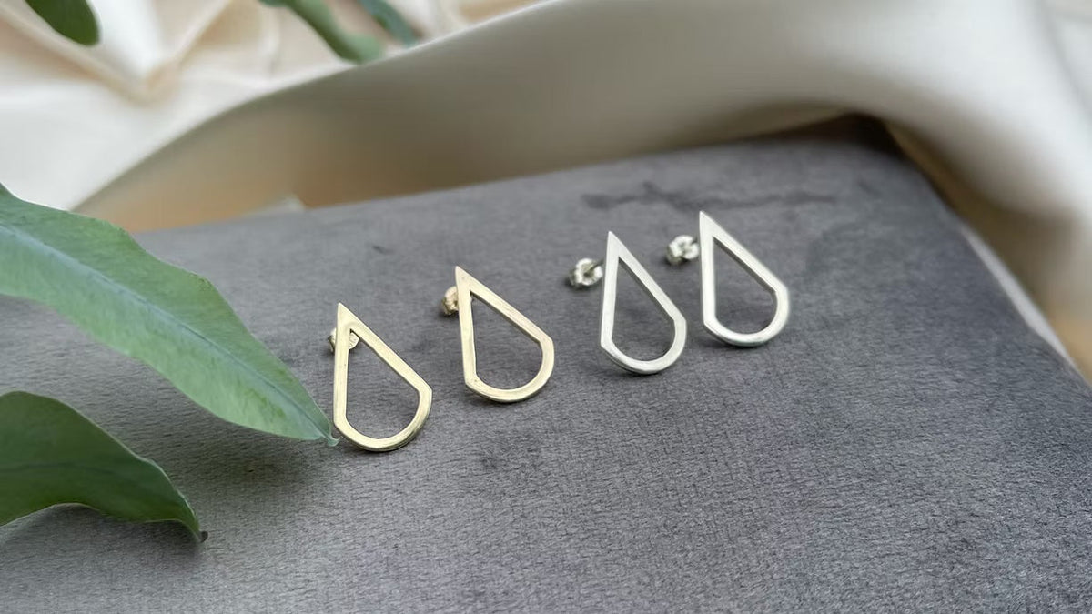 Gold teardrop-shaped earrings on a gray surface with green leaves.