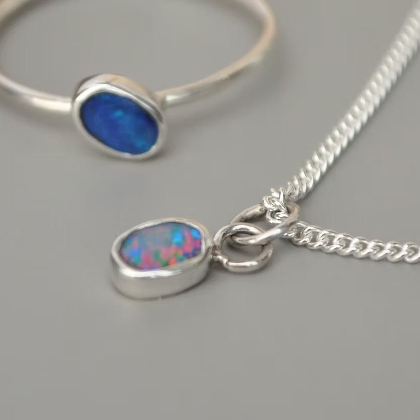 A sterling silver necklace with a curb chain and a teardrop-shaped blue opal pendant, shown alongside a matching silver bangle bracelet on a neutral gray background.